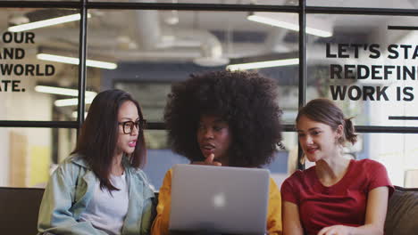 Drei-Millennial-Frauen-Bei-Einem-Ungezwungenen-Treffen-In-Einer-Bürolounge,-Die-Gemeinsam-Einen-Laptop-Nutzen,-Schrägaufnahme