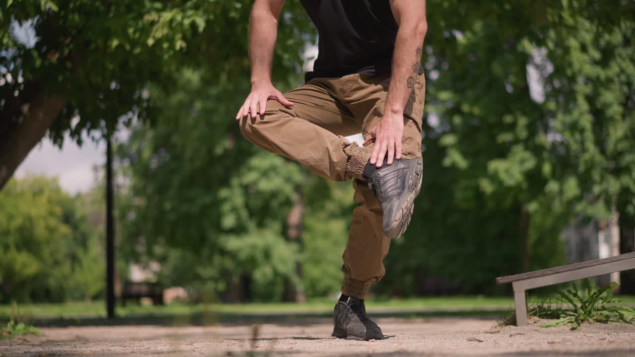 Individual Maintaining Balance In Casual Attire, Person Carefully Balancing On One Leg During Summer Walk, Calm Man In Casual Clothing Executing Careful Onelegged Stance On Park Walkway
