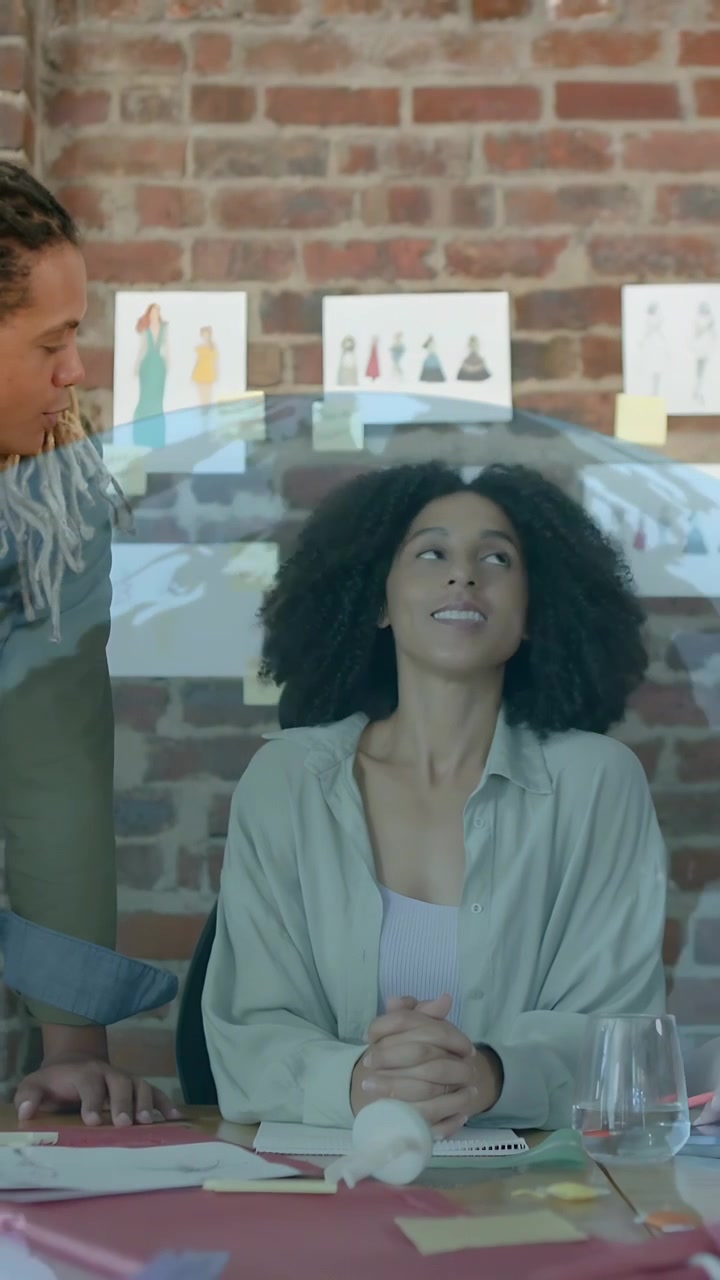Vídeo vertical: Mulher sentada, homem inclinado gesticulando, adicionando grades holográficas e ícones de globo, revisando moda.