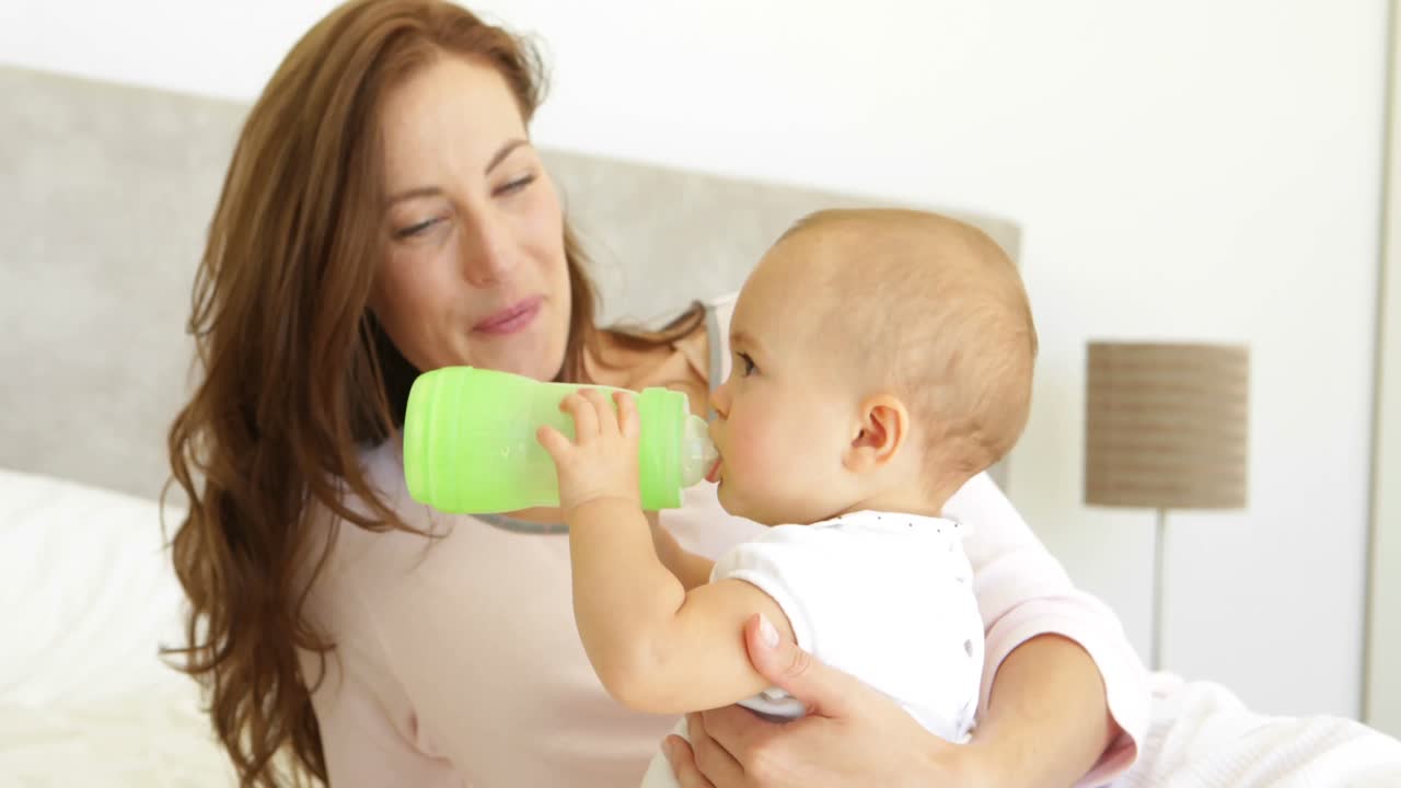Giovane madre sorridente che guarda la sua bambina bere dal biberon