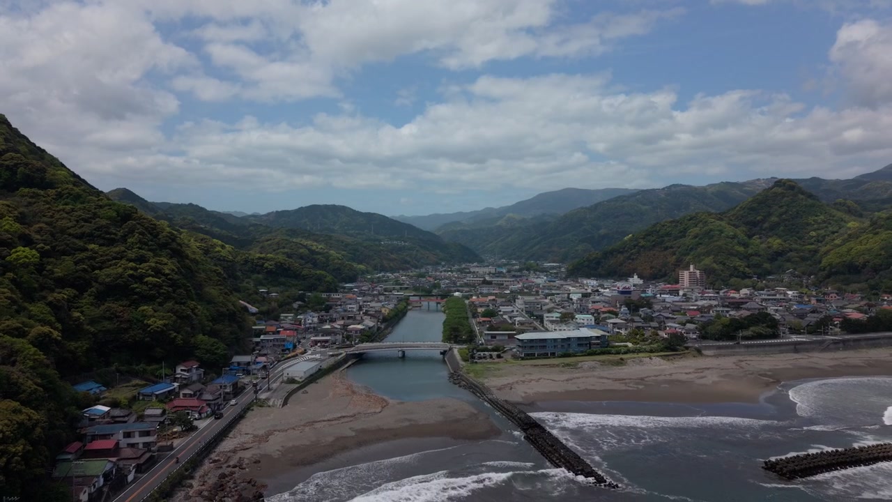 River mouth opening onto a sandy beach beside a mountain valley town in Kawazu, Izu, Japan, at midday, wide shot from an elevated viewpoint