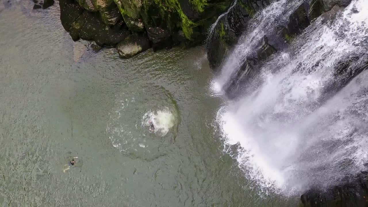 joven acróbata saltando desde un acantilado cerca de una cascada, en el río doubs, suiza