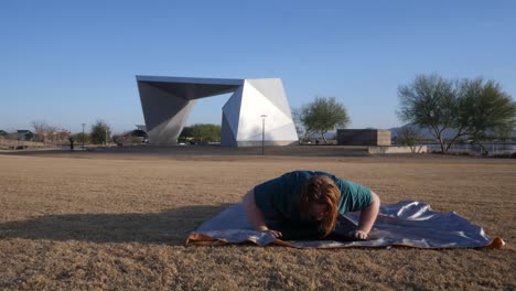 Overweight red hair male doing push ups in a park with an amphitheater behind them.