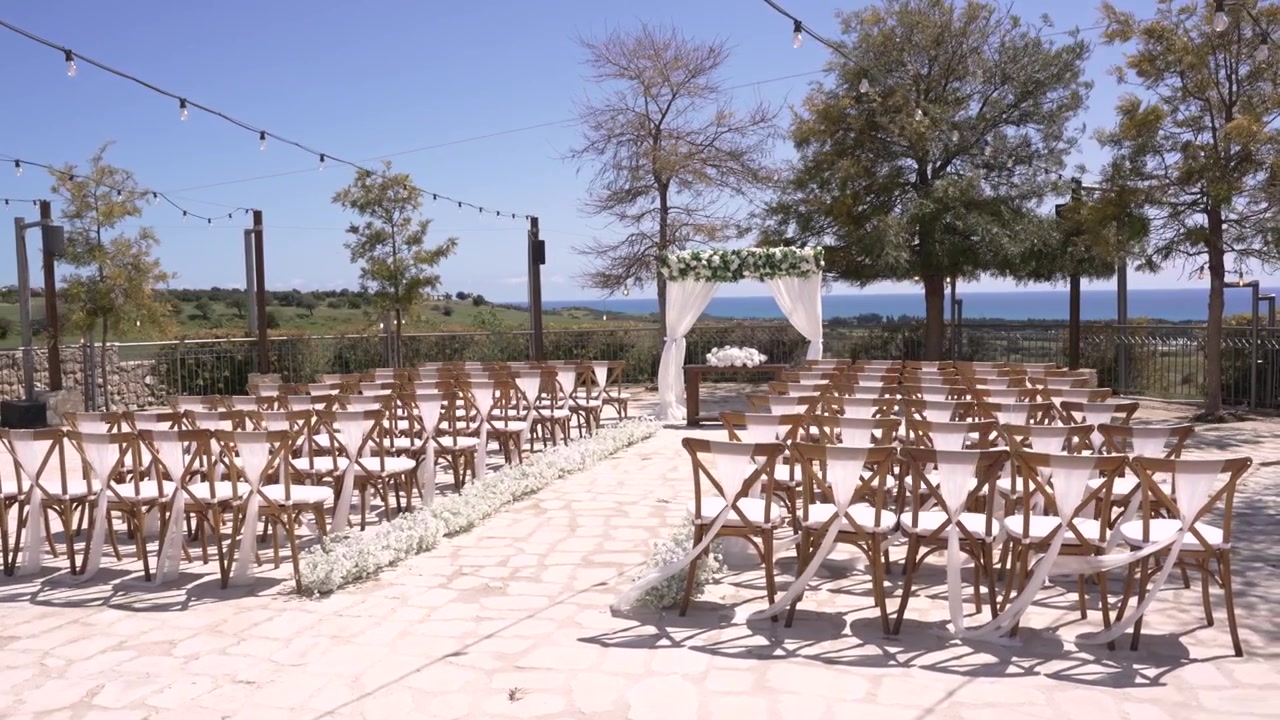 Sedie disposte per una cerimonia nuziale in un'area esterna. Decorazioni bianche sono allestite di fronte a una splendida vista. L'evento è previsto per una giornata di sole in un ambiente di campagna