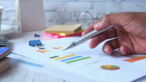 side view of man hand with pen analyzing bar chart on paper