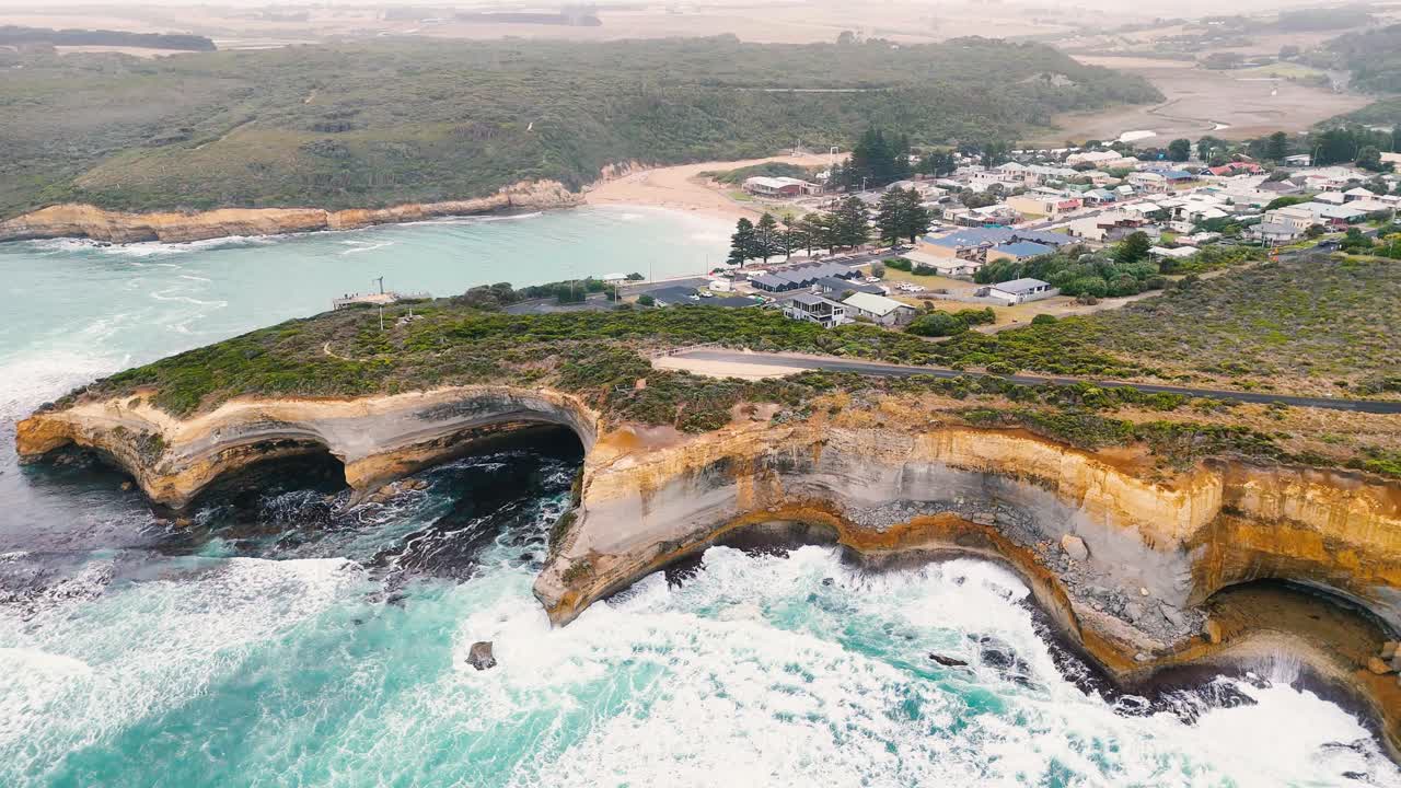 Drone footage captures Port Campbell's dramatic cliffs and turquoise waves under soft, natural lighting. The camera smoothly glides over the scenic landscape