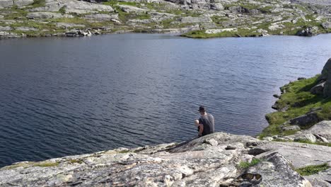 man sitting on rock fishing in mountain lake while on camping trip