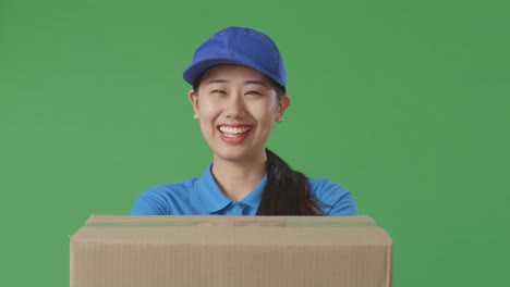 close up of asian female courier in blue uniform showing a carton to camera and smiling while delivering it on green screen background in the studio