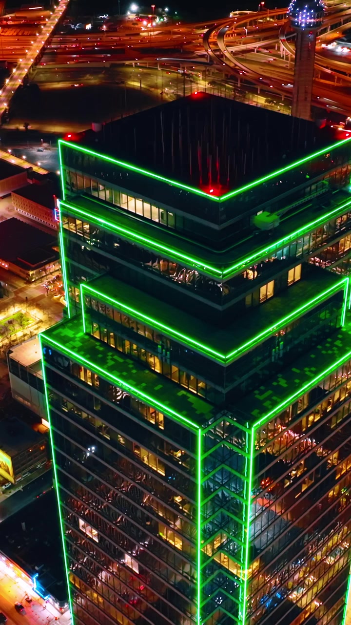 Imagens do topo do Bank of America Plaza com iluminação de argônio verde percorrendo principalmente as bordas e cantos da torre. Vista luminosa de Dallas do alto. Vídeo vertical.