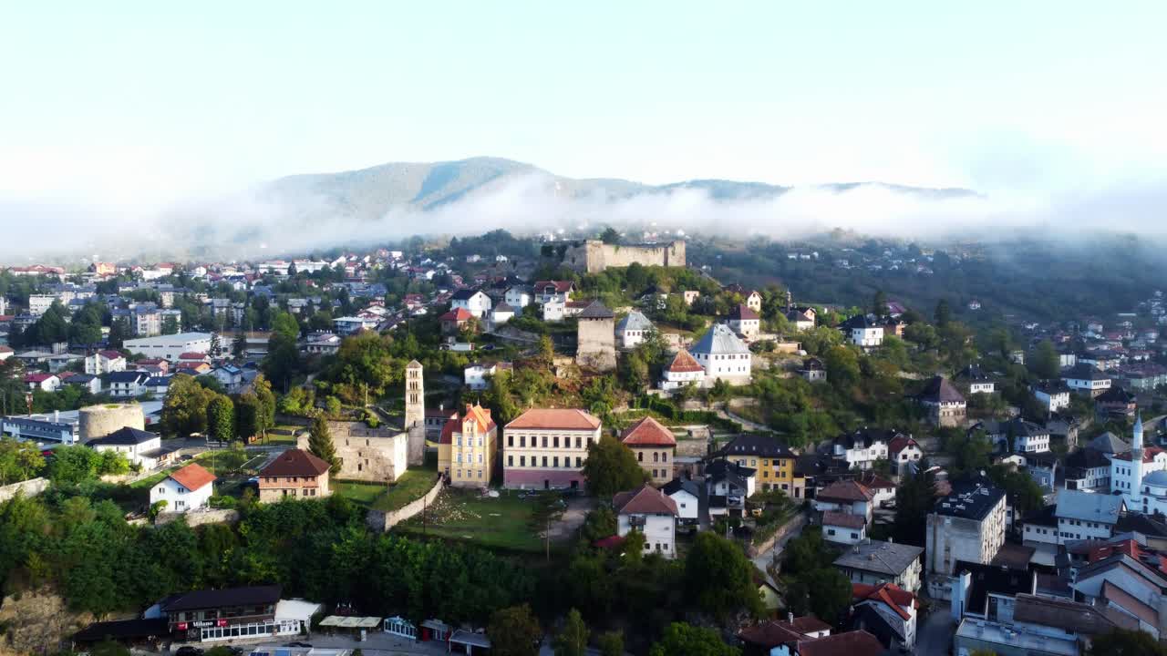 Vista cinematografica aerea con drone della città di Jajce all'alba, Bosnia ed Erzegovina. La calda luce del primo mattino, le colline nebbiose e il paesaggio urbano storico creano un'atmosfera di viaggio e turismo serena.