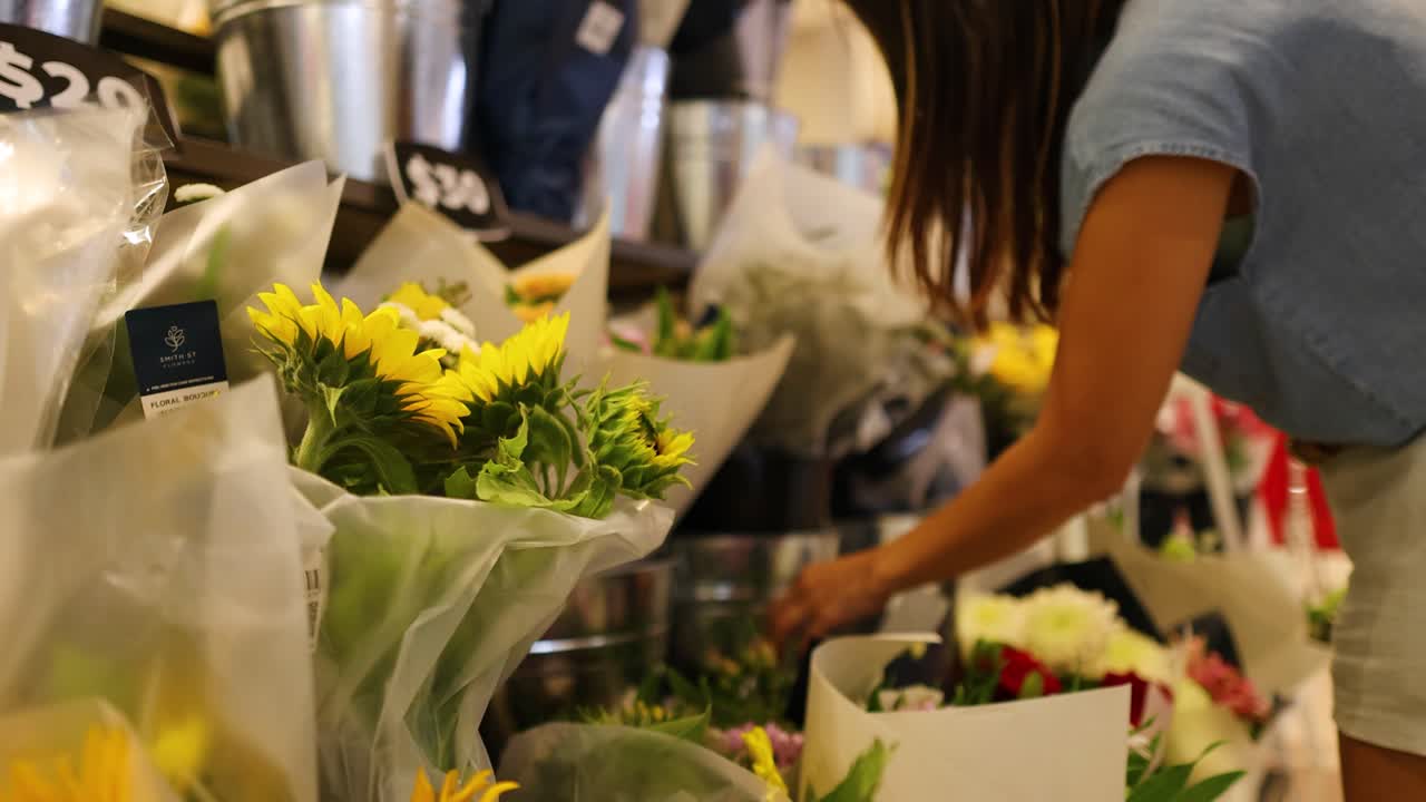 A woman in a blue shirt and shorts chooses sunflowers in a well-lit Gold Coast flower shop