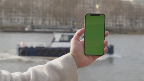 close up of man holding green screen mobile phone looking out to river thames and embankment in london uk 1