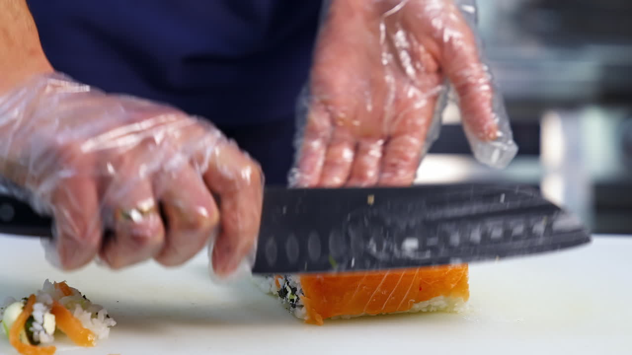 Chef cuts sushi with sharp knife into pieces. The process of sushi cooking, preparing. Japanese cuisine concept.