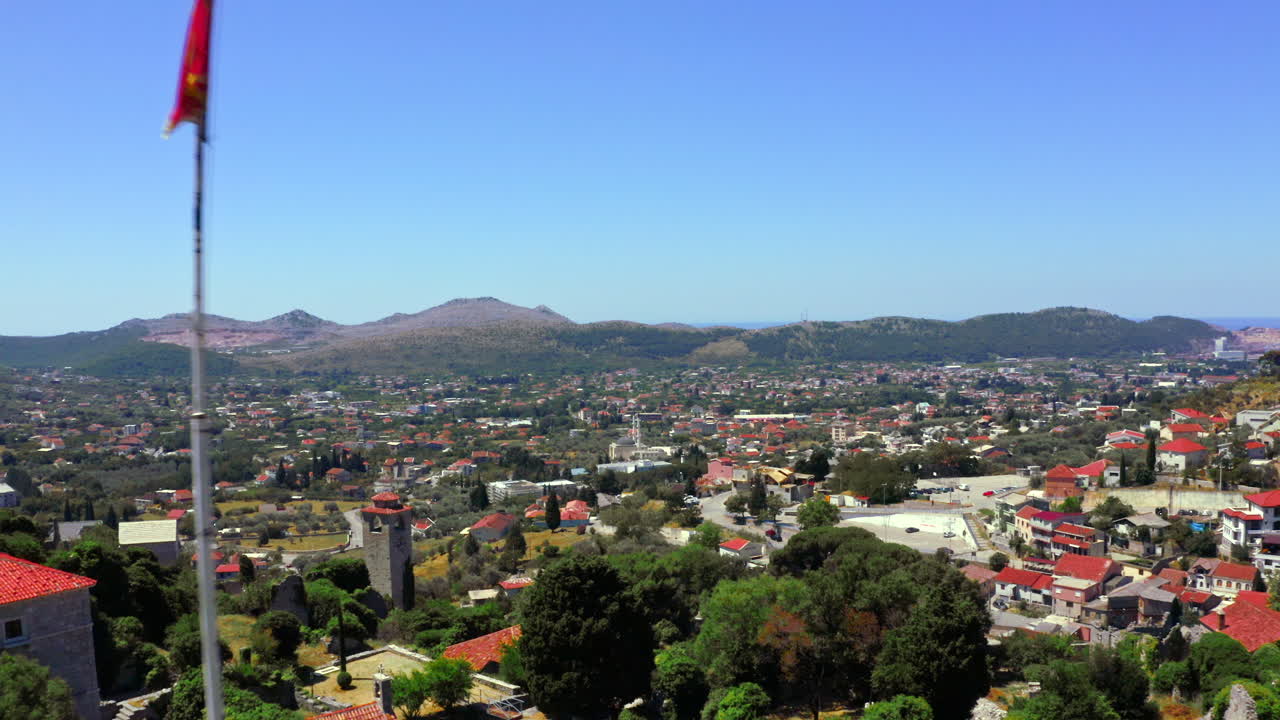 toma aérea de zoom de 4k de la fortaleza de stari bar con una bandera de montenegro en sus paredes y una vista de la ciudad de bares en un día soleado de verano sin nubes
