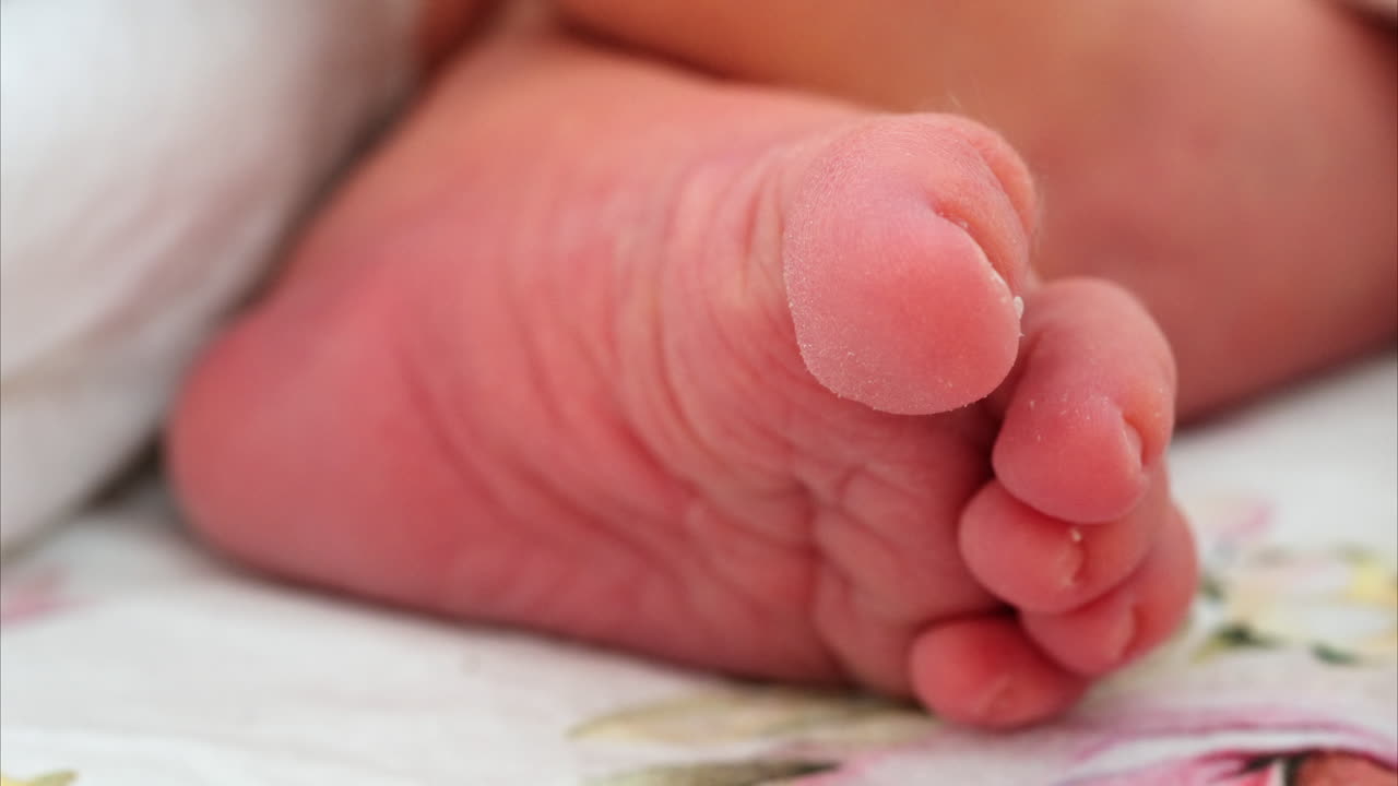 Nærbillede af foden på en nyfødt baby, der hviler på hvidt sengetøj med forskellige mønstre