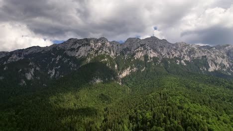 lush forest at the base of the towering piatra craiului mountains, clouds casting shadows