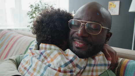 loving african american dad and little son embracing on sofa at home