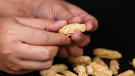 hands peeling peanuts over a black background