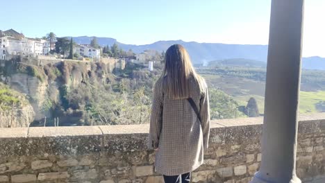 hand-held shot of a young woman walking towards a wall and resting in ronda, spain