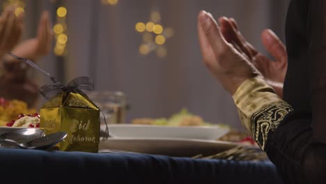 close up of muslim family sitting around table at home saying prayer before biryani is served celebrating eid