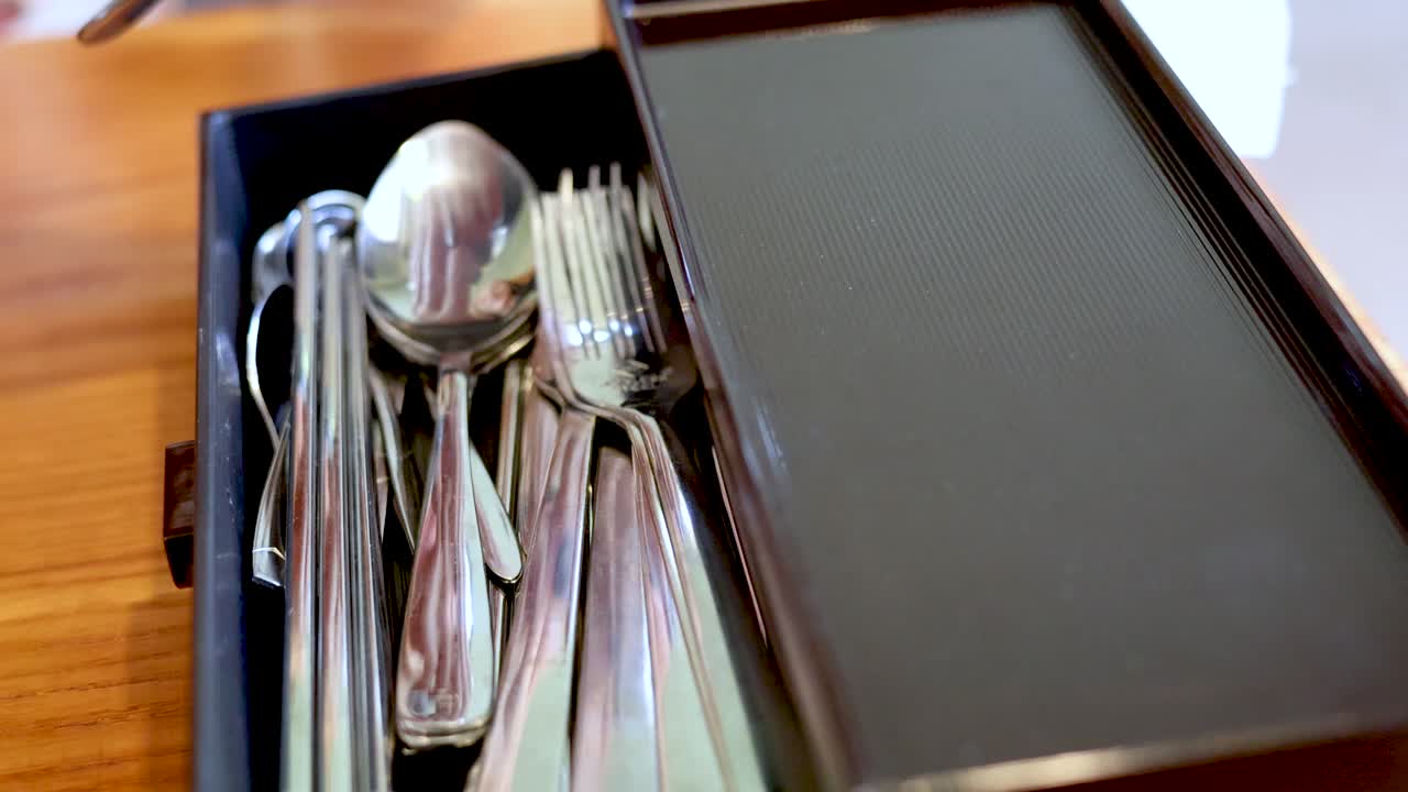 A woman opens a kitchen drawer and selects a shiny metal spoon from organized silverware