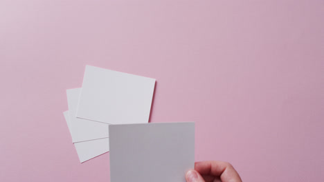 hand holding piece of paper over pieces of paper with copy space on pink background in slow motion