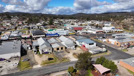 drone camera smoothly pans above stanthorpe, queensland, revealing small-town residential homes, parked cars, and local businesses under bright daylight with scattered clouds