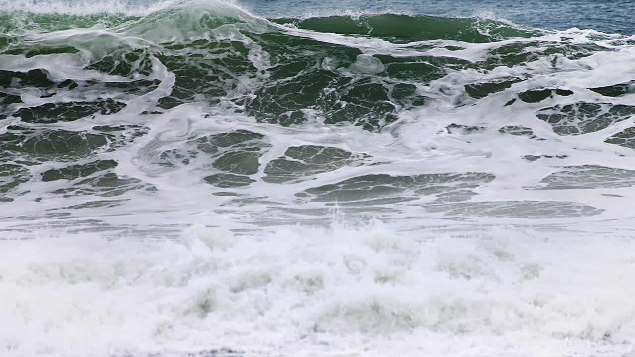 120fps 4k 푸티지에서 고속 카메라 120fps 4k 푸티지 뒤에 깊은 짙은 파란색 바다가 있고 흰색 물이 쏟아지는 해안에서 느린 동작으로 충돌하는 관형 파도를 찾는 빠른 팬
