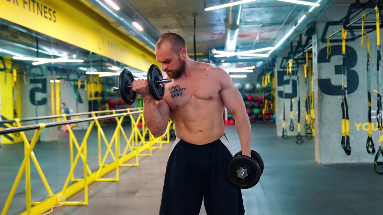 Uomo muscoloso che esegue curl bicipiti con manubri in una palestra moderna