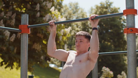 Athletic caucasian topless muscular man doing pull ups exercises on horizontal bar pumping up back
