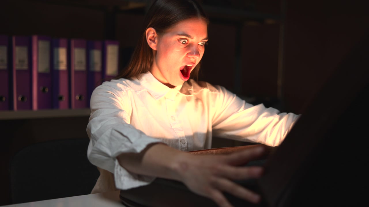 Una valigia nera poggia su un tavolo in primo piano, con una chiusura metallica e un guscio curvo visibili, mentre una persona appare leggermente sfocata sullo sfondo.