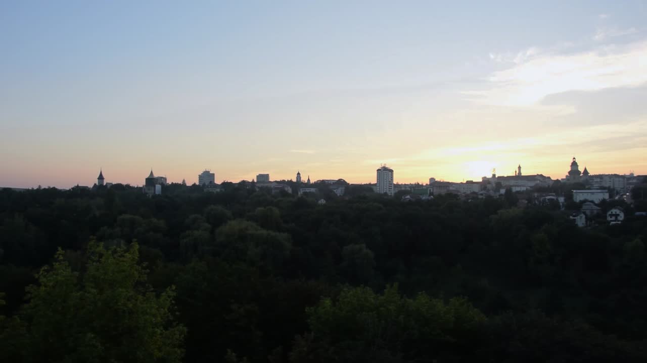 Panorointikuva kaupungin siluetista auringonlaskun aikaan, paljon puita etualalla.