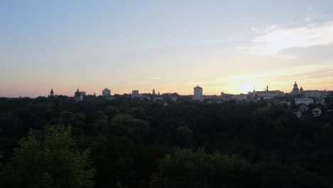 panning shot of the skyline of a city at sunset, with lots of trees in the foreground