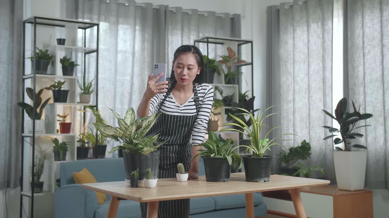 아시아 여성이 집에서 스마트폰으로 식물 판매를 라이브 스트리밍하는 동안 손을 흔들고 이야기합니다.