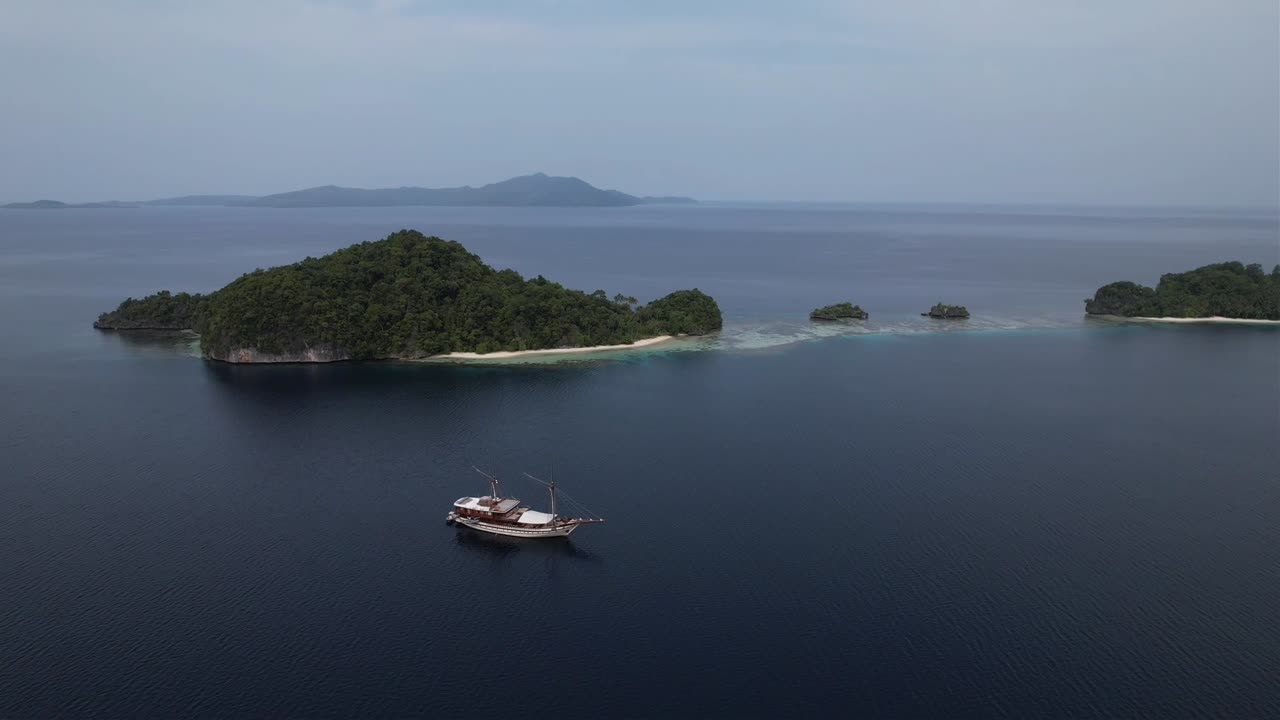 View on beautiful island with crystal clear waters, white sand beaches, coral reefs and phinisi ship in Raja Ampat, Wofoh Area, Indonesia