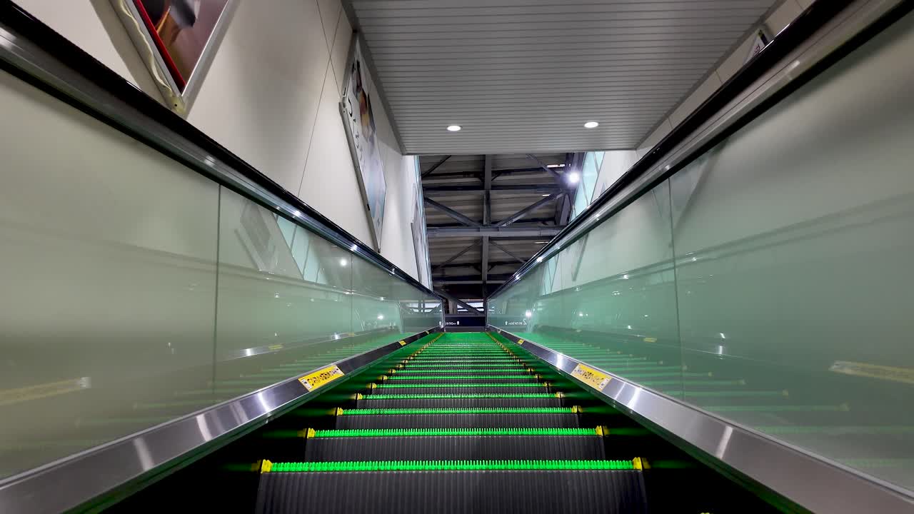 Riding up an escalator at Toyama Station in Japan, surrounded by vibrant green neon lights and sleek modern architecture