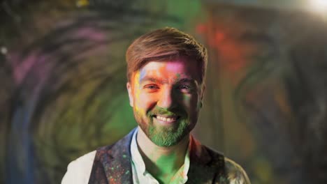 close-up portrait of an artist with a painted face with colored paints who covers half of his face with his hand and smiles