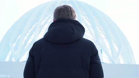 man looking at a dome-shaped building in winter