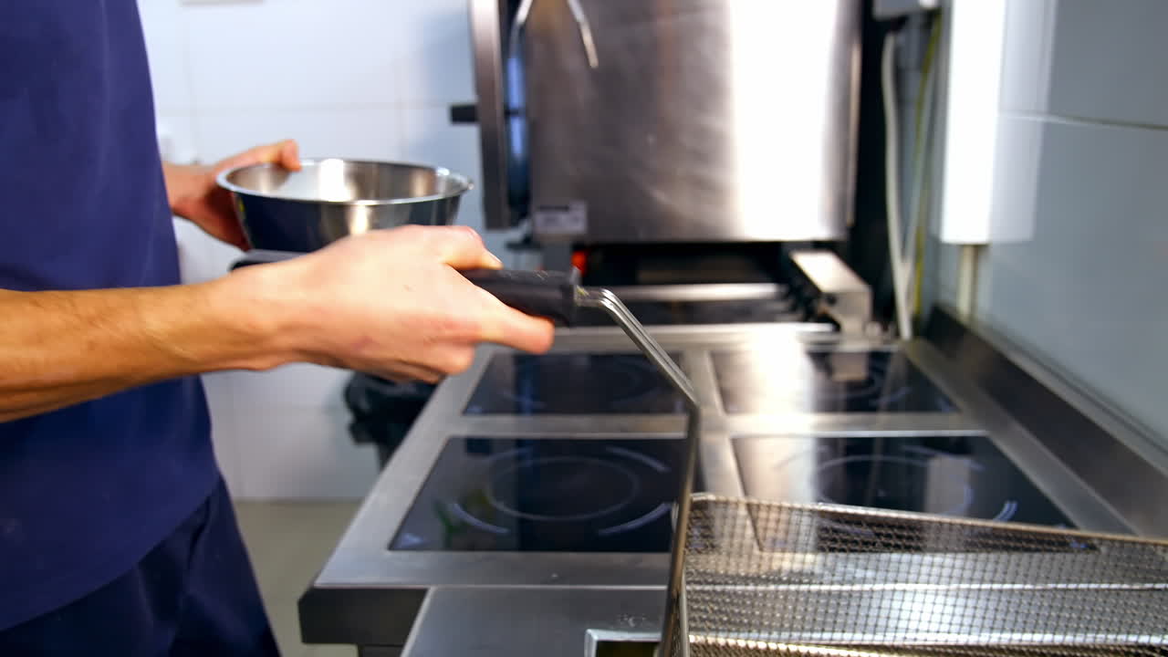 Ready french fries put into big stainless steel bowl. Professional kitchen background in modern restaurant. Potatoes fried in oil.