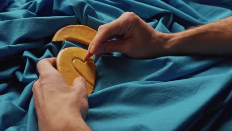 men's hands break sugar cookies candy in the shape of a heart.