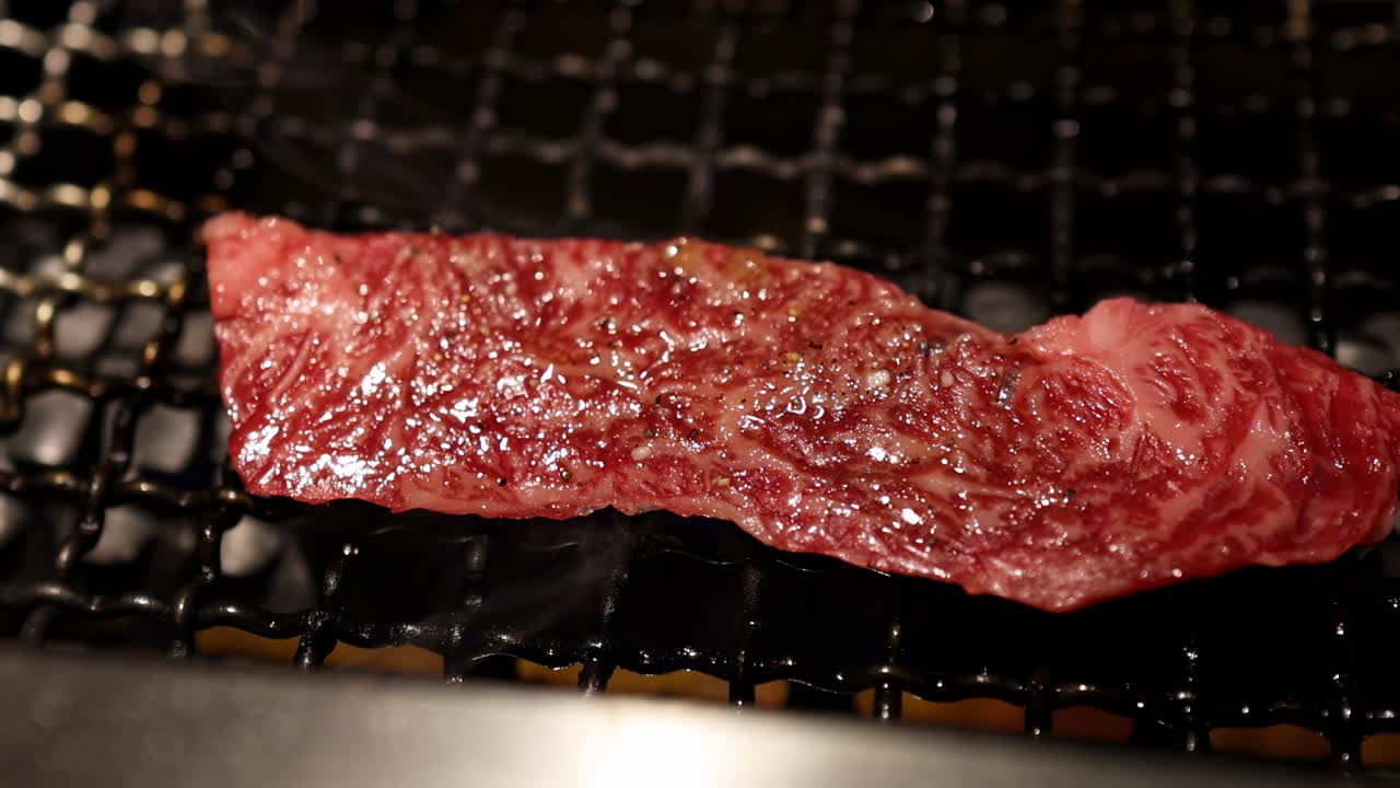 Detailed view of a marbled steak sizzling on a wire rack, highlighting texture and browning process.