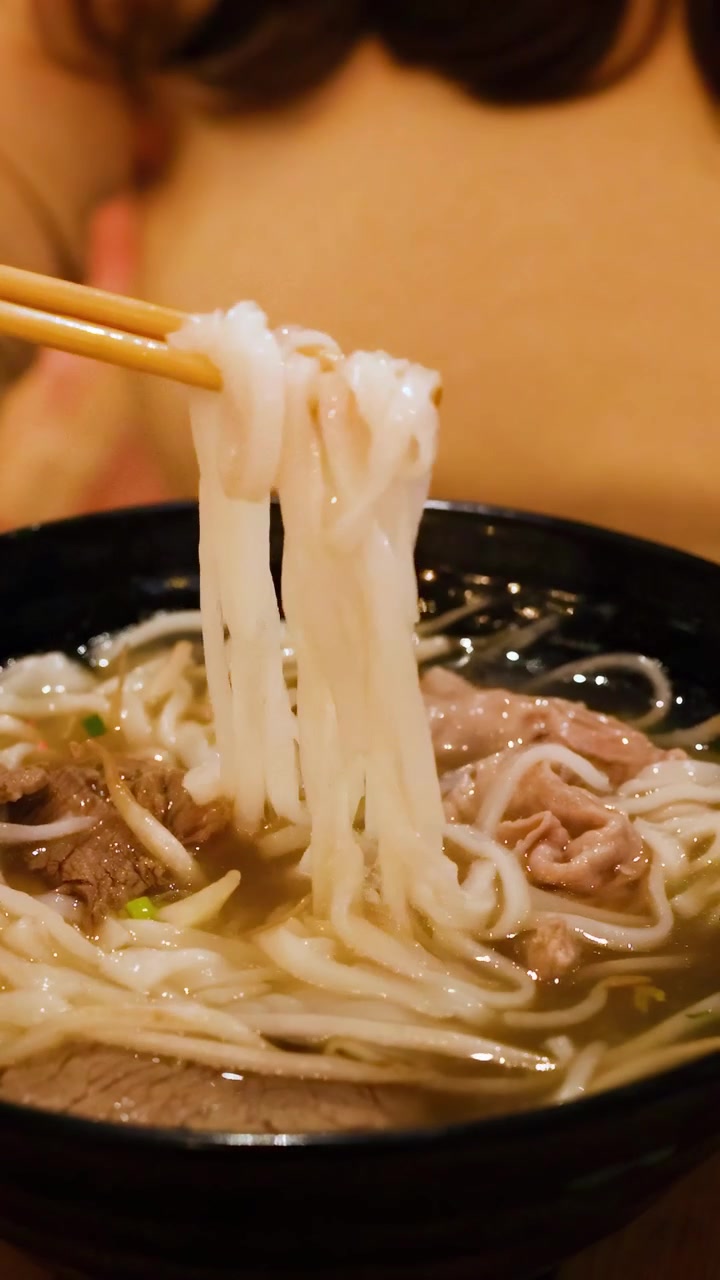 Una persona usa abilmente bacchette e cucchiaio per gustare una ciotola di pho vietnamita in un ambiente accogliente