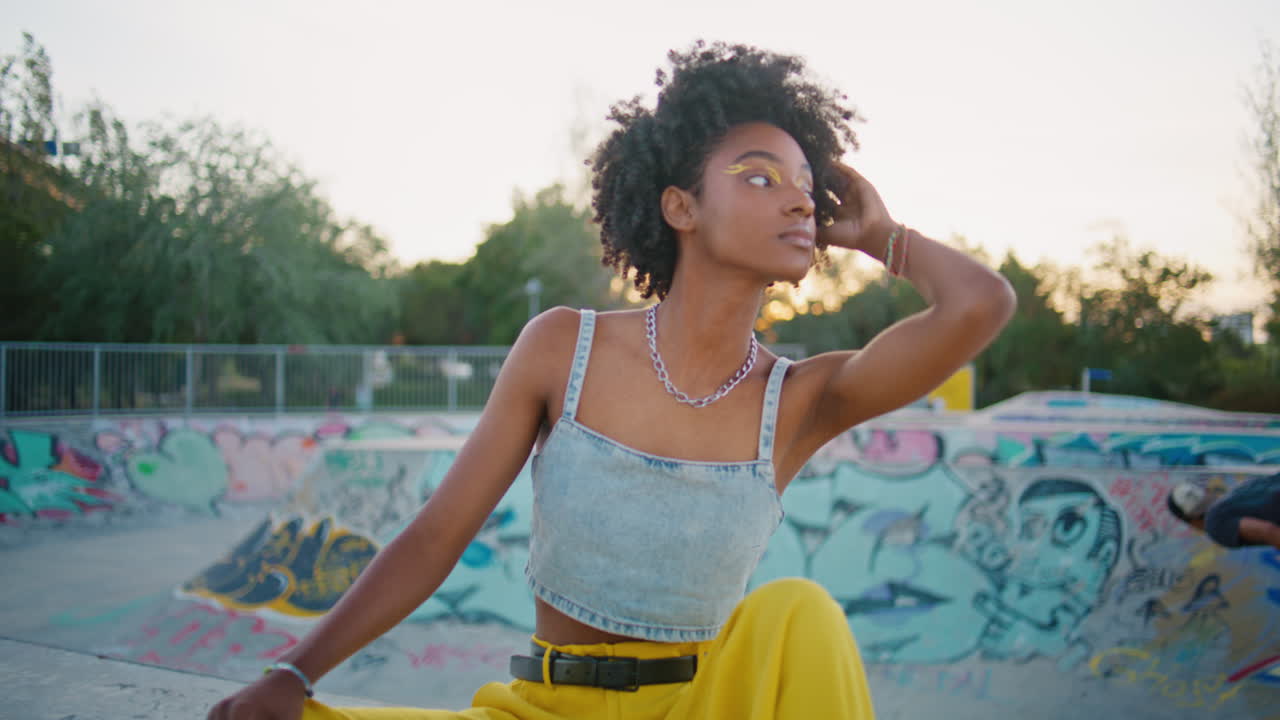 cool hipster sentado en la tabla de patinaje relajándose en el parque de patinadores de cerca. chica