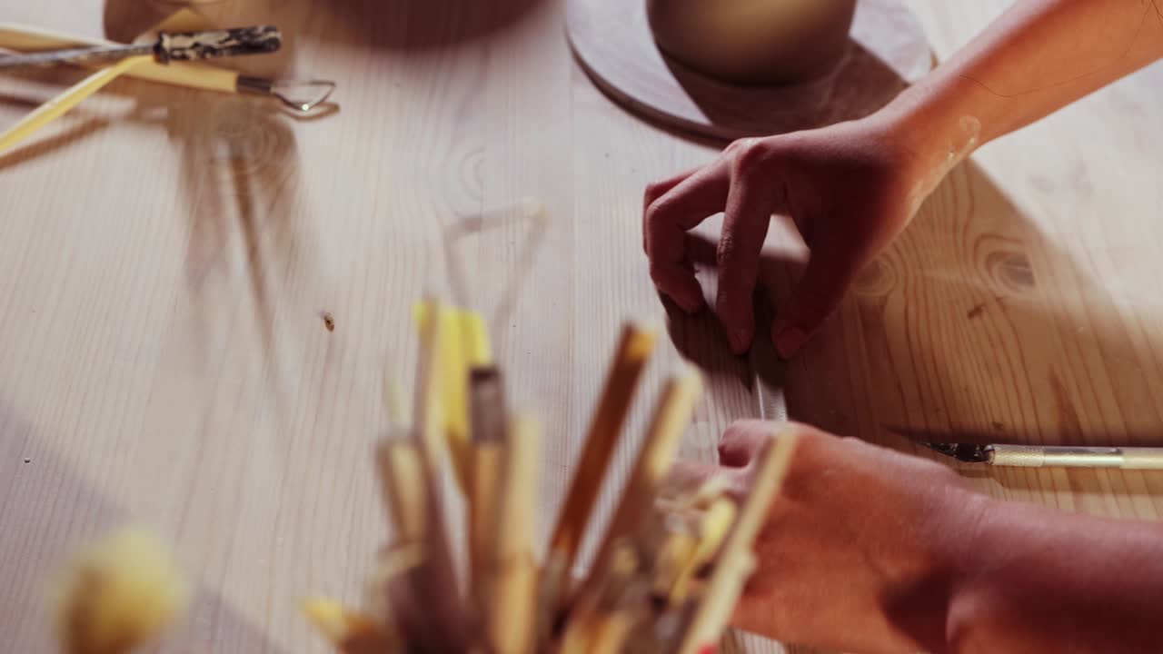 cerámica en el estudio - mujer alfarera corta un pequeño pedazo más largo de arcilla