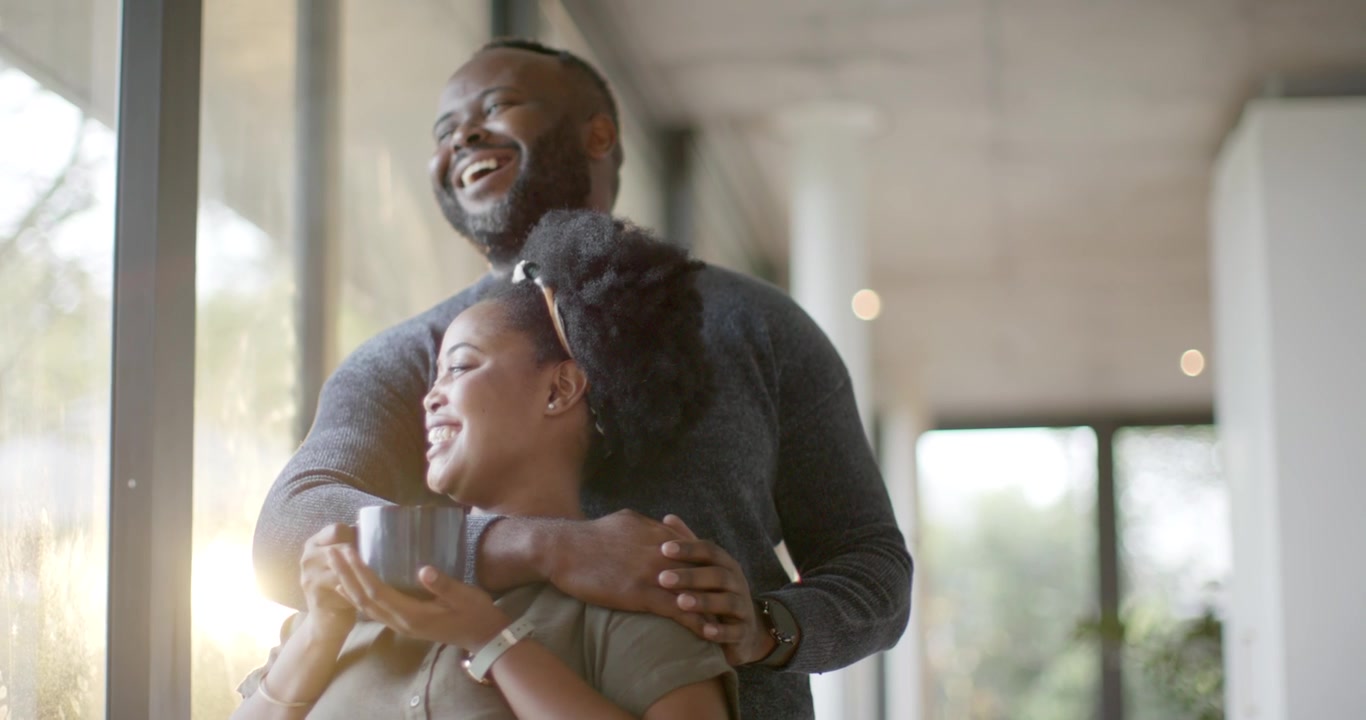 African American couple leaning by window man coming embracing woman with mug sharing morning light