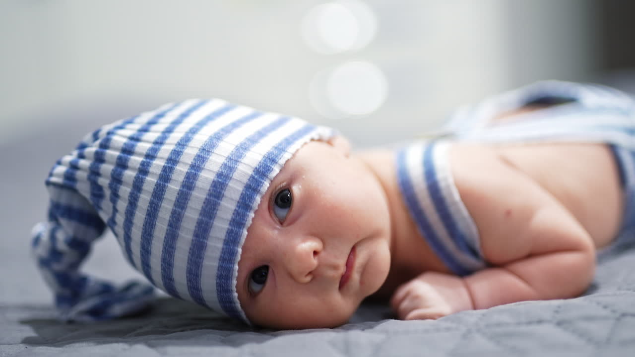 Curious little boy in blue and white hat trying to hold his head up. Sweet child I a funny suit lying on his belly. Close up.