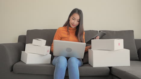 Schöne-Asiatische-Frau,-Die-Zu-Hause-Ipad-Tablet-Und-Laptop-Auf-Der-Couch-überprüft