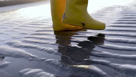 Gelbe-Stiefel,-Die-Bei-Sonnenaufgang-In-Zeitlupe-An-Einem-Sandstrand-Spazieren-Gehen