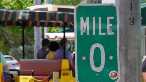 the mile marker 0 sign at the end of us highway 1 in key west florida and a tour train drives by in the background, slow motion.
