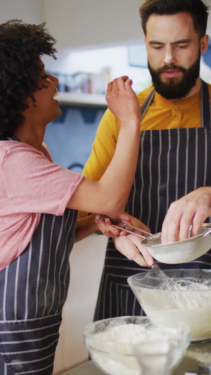 Vertical video of happy diverse couple baking in kitchen, having fun with flour, with copy space